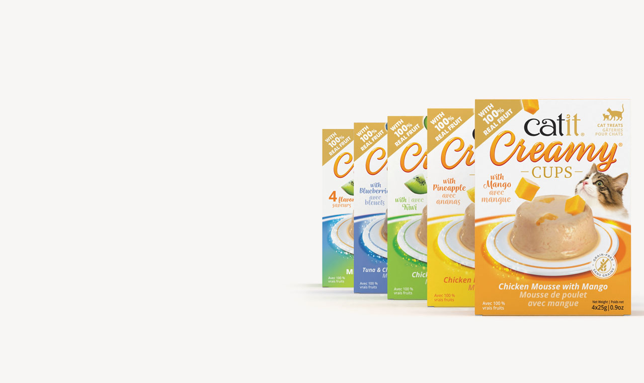 Five packages of Catit Creamy Cups cat treats arranged in a row, featuring various fruit-infused mousse flavors
