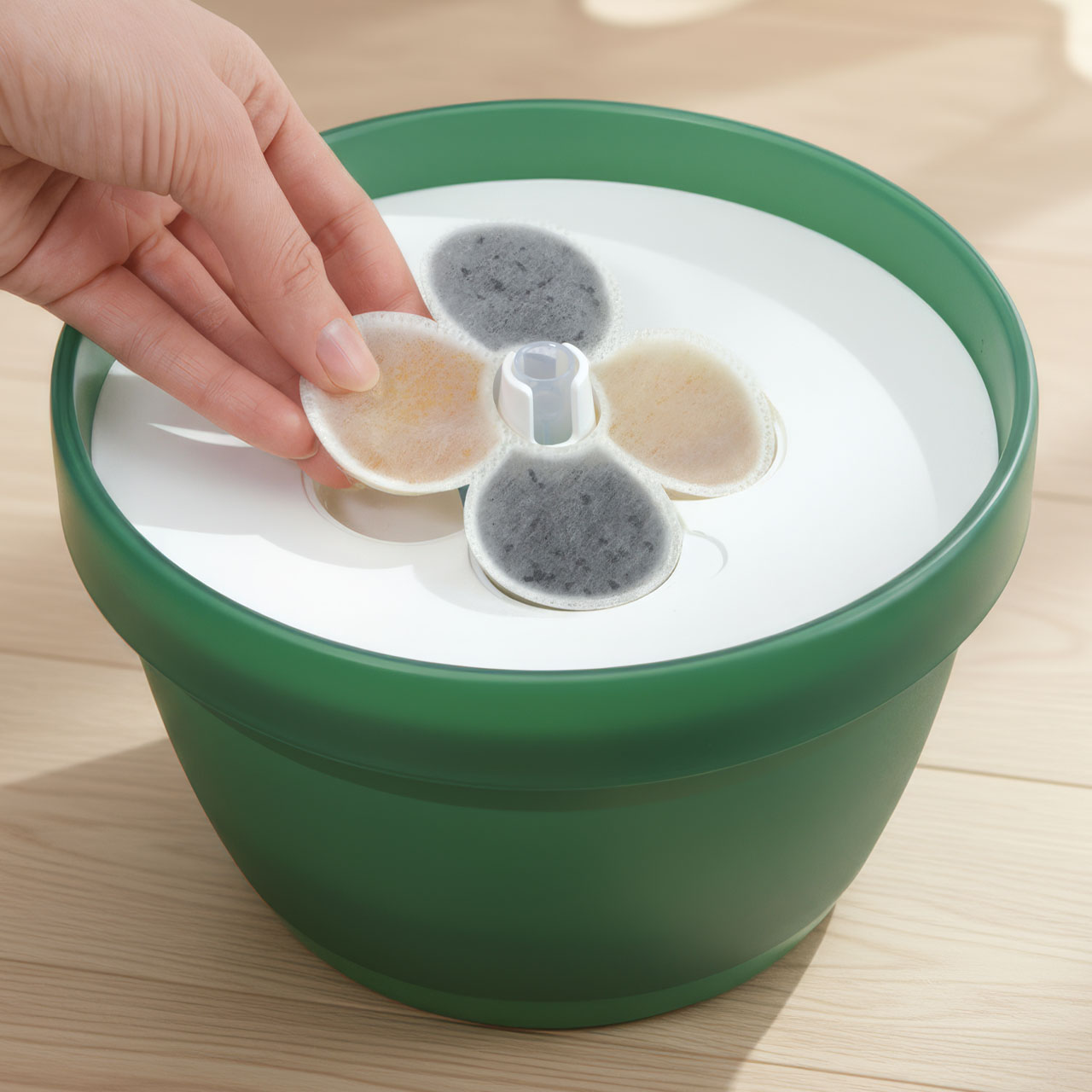 A hand placing a circular filter into a green Catit flower water fountain for cats
