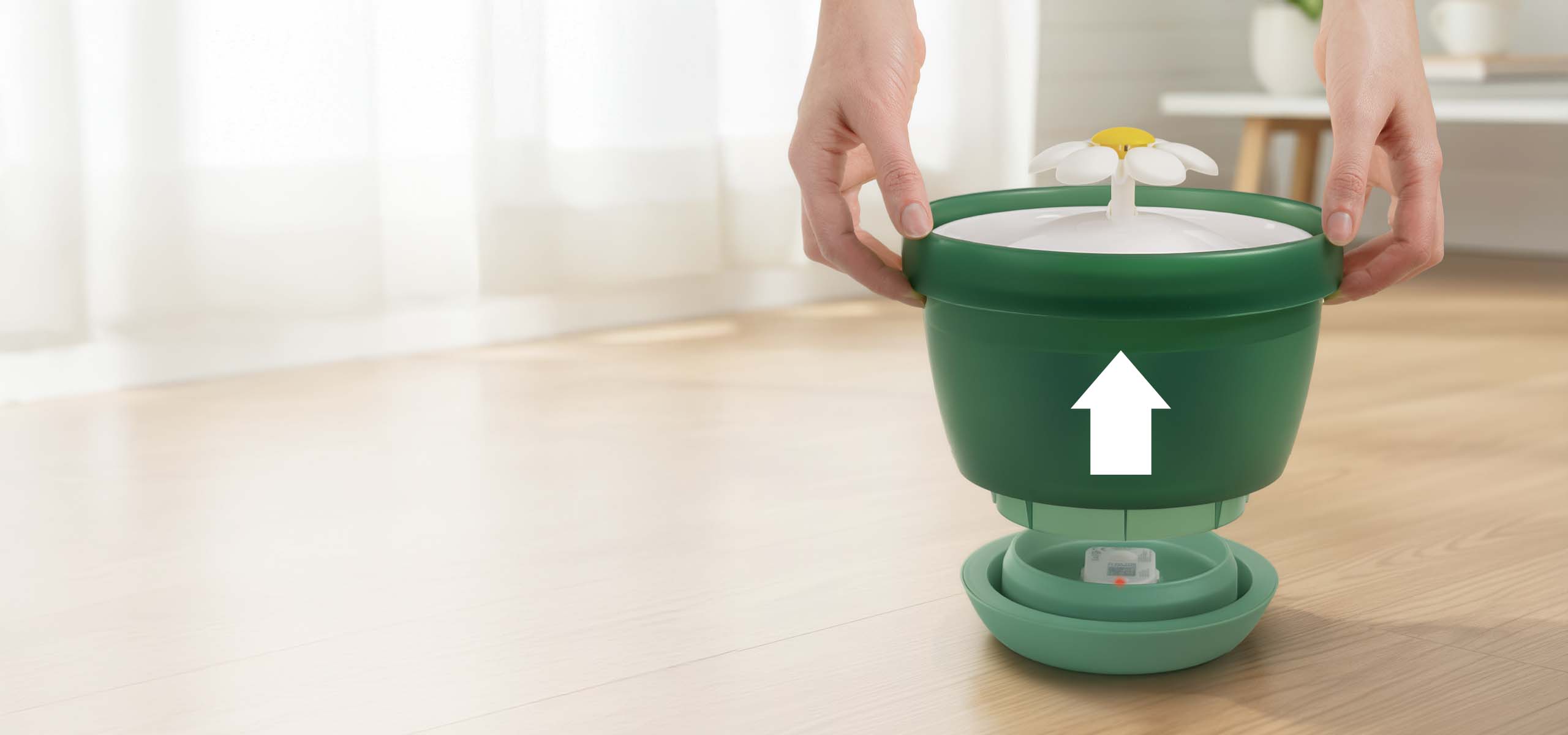 Hands lifting the green top section of a Catit flower water fountain off its base