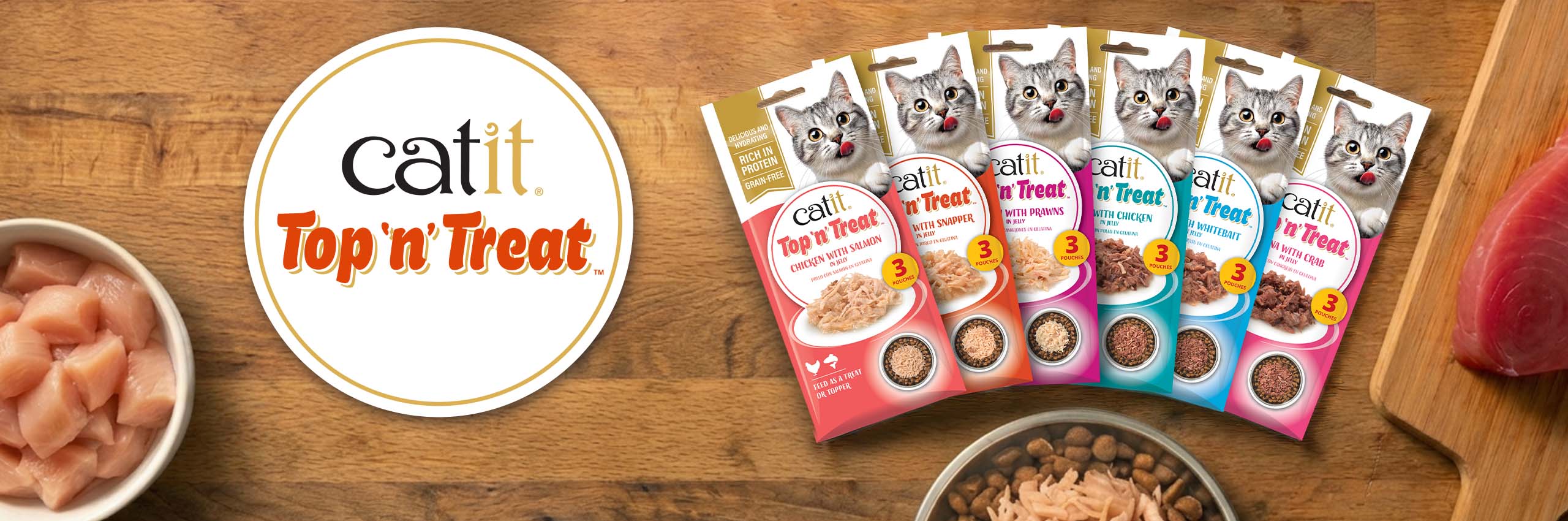 Catit Top 'n' Treat cat food pouches in various flavors displayed on a wooden surface with raw ingredients