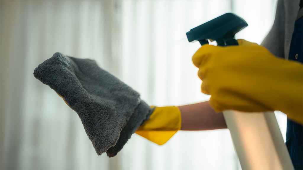 Een persoon met gele rubberen handschoenen spuit water op een microvezeldoek.