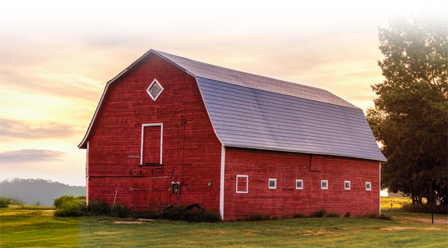 A red barn sits in a grassy field under a sunset sky