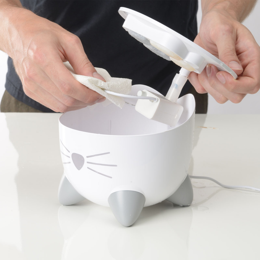 Hands taking of top of PIXI mini fountain and cleaning the cable with a paper towel