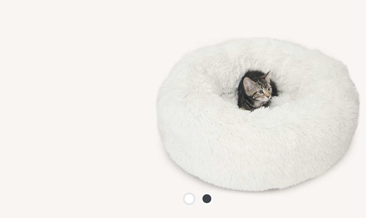 A tabby kitten sitting inside a round, white, fluffy cat bed