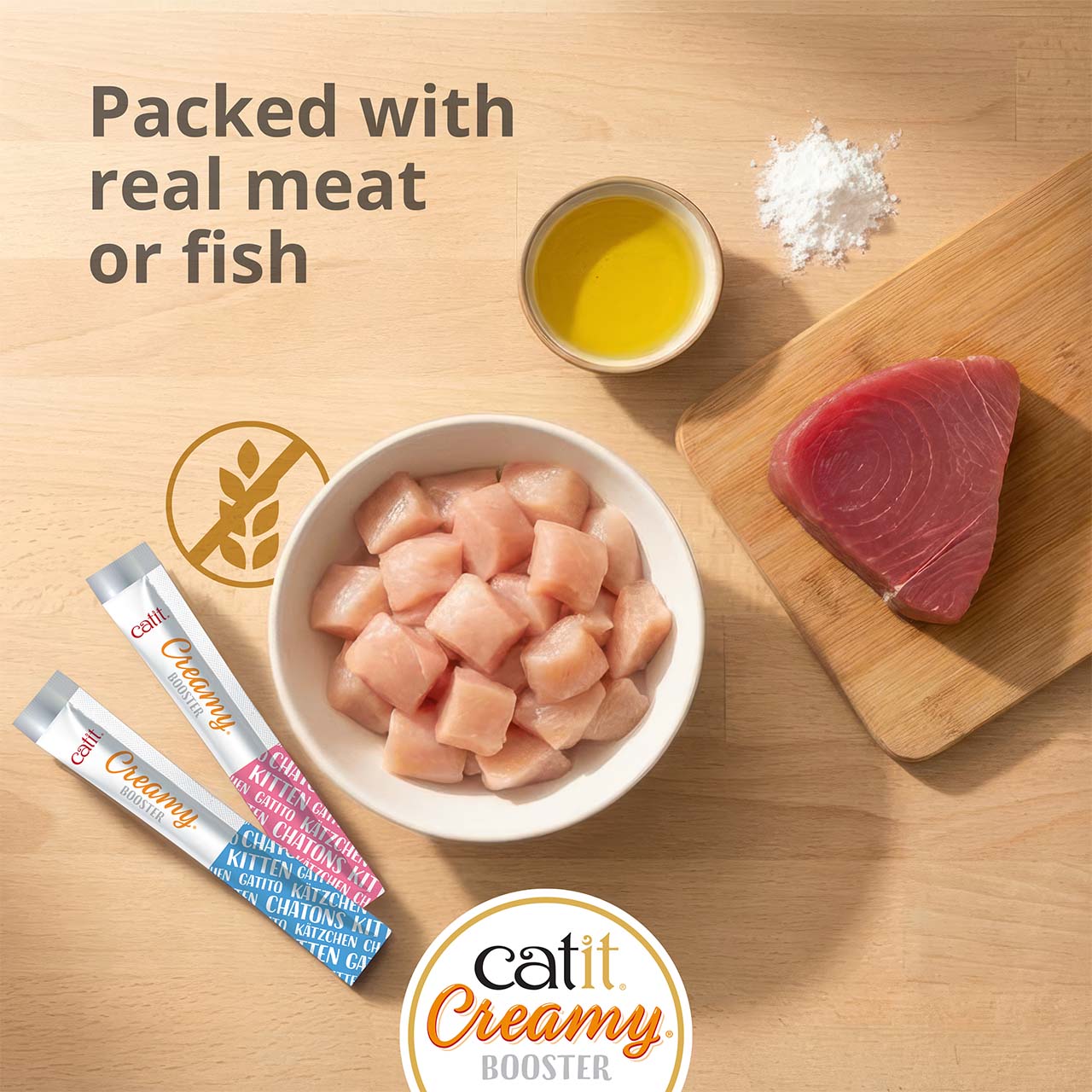 Bowl of cut chicken, tuna on wooden board laying on wooden countertop with two Catit Creamy Booster Kitten tubes