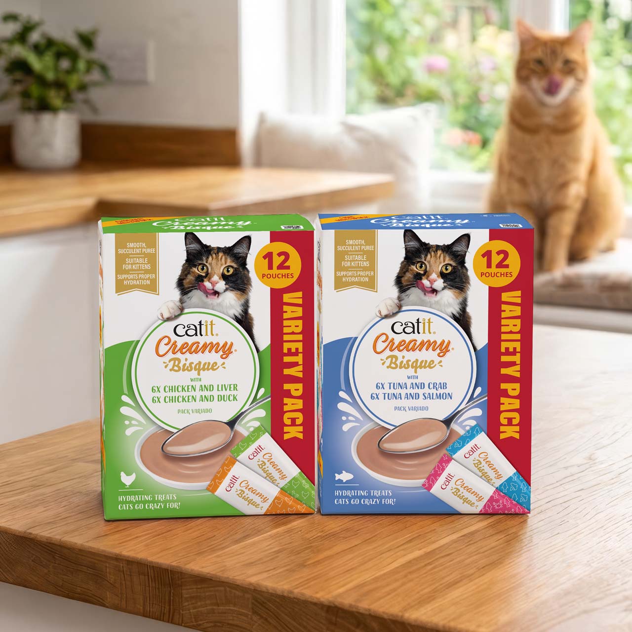 Catit Creamy Bisque Multipacks on a wooden kitchen counter with in the background a ginger cat licking it's face