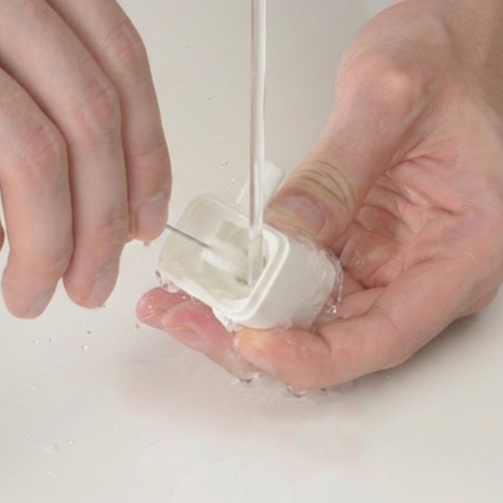 Hands cleaning inside of the PIXI Mini Fountain pump with brush