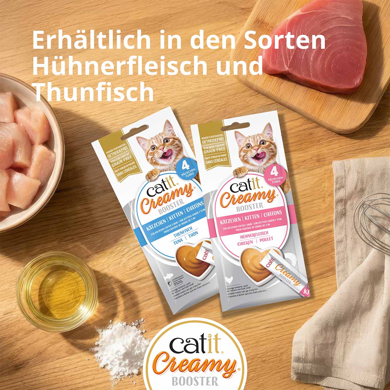 Verpackungen von Catit Creamy Booster Kitten liegen auf einer Holzarbeitsplatte, umgeben von Zutaten; Ansicht von oben.
