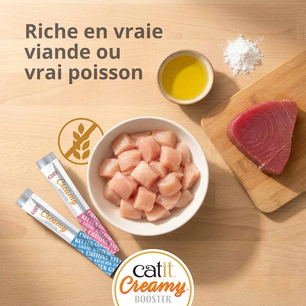 Bol contenant des morceaux de poulet et du thon posé sur une planche en bois sur un plan de travail en bois, avec deux tubes de Catit Creamy Booster Chatons