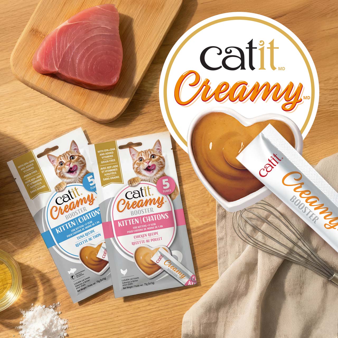 Gâteries à lécher Catit Creamy Booster pour chatons, à saveur de thon et de poulet, disposées sur un comptoir en bois avec des ingrédients